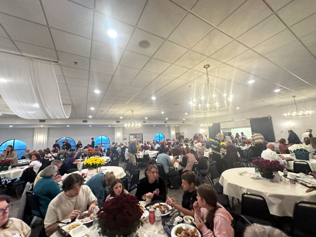 Dining room filled with circular tables with white tablecloths, nearly every table filled with people at the Greek Food Bazaar in Reading, PA.