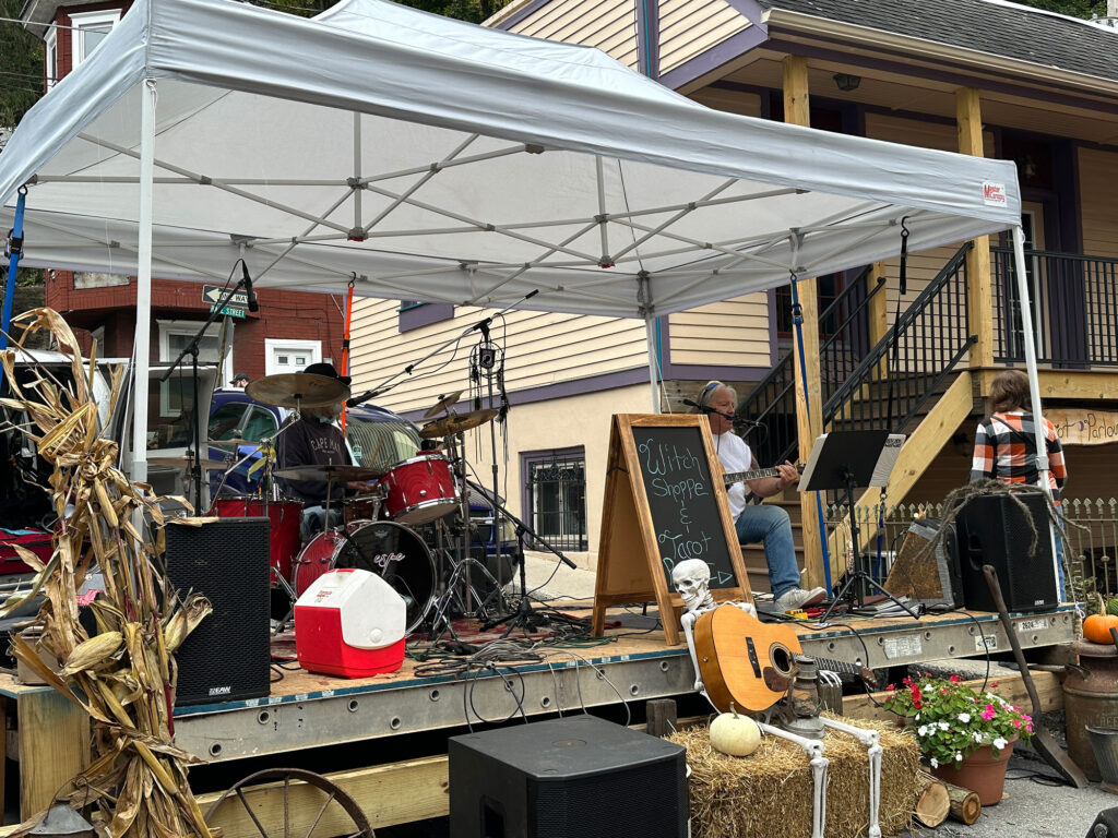 makeshift festival stage with two older men, one playing drums behind a red drumkit and another in white t-shirt and jeans playing acoustic guitar