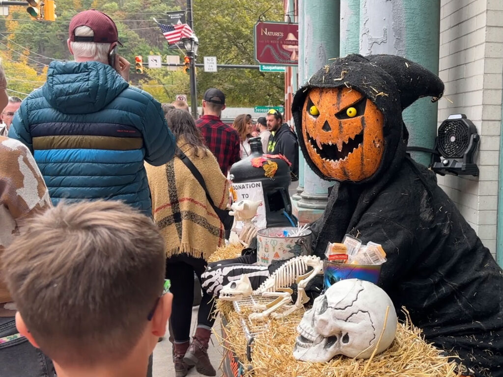 A young boy walks up to a man wearing a pumpkin mask outside a storefront in Jim Thorpe, PA.