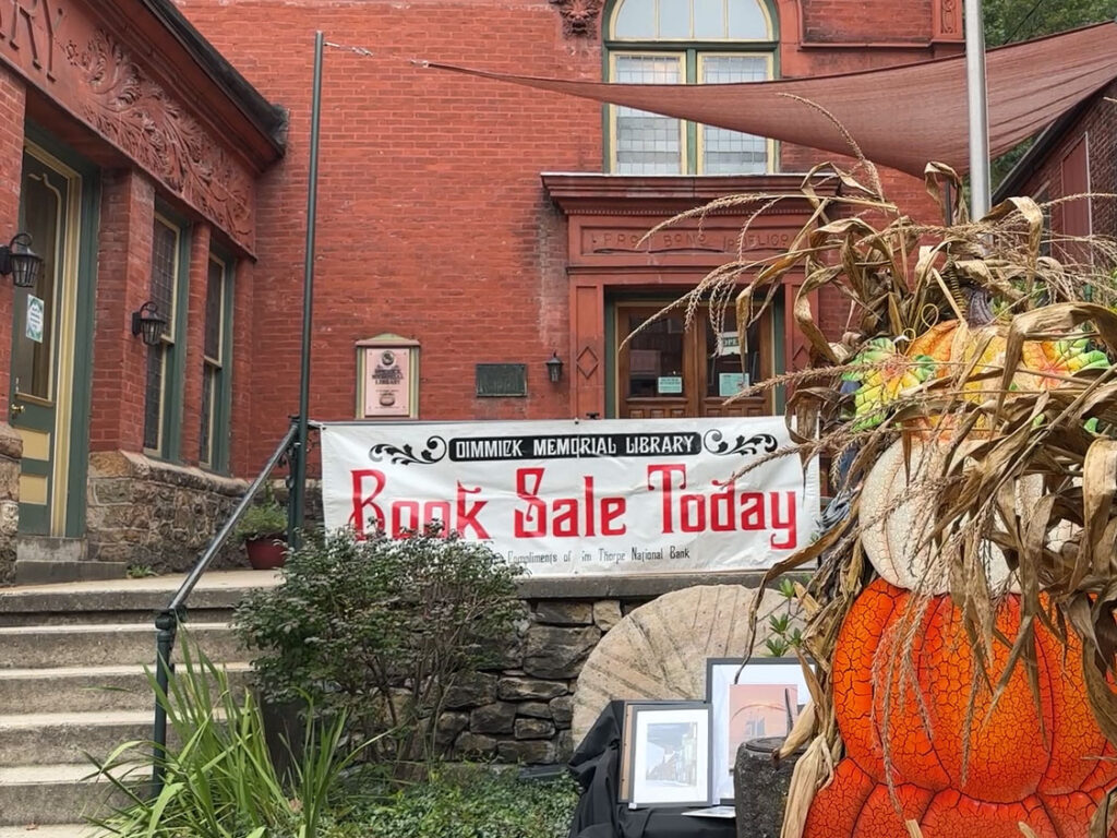 sign hanging from a railing in front of a brick building. The sign reads "Book Sale Today"