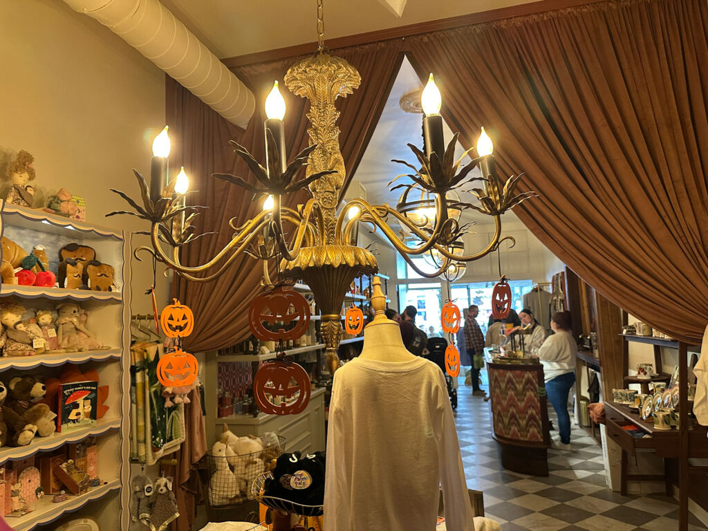 antique chandelier with eight candle-shaped light bulbs in a yellow-lit room with a pulled back curtain
