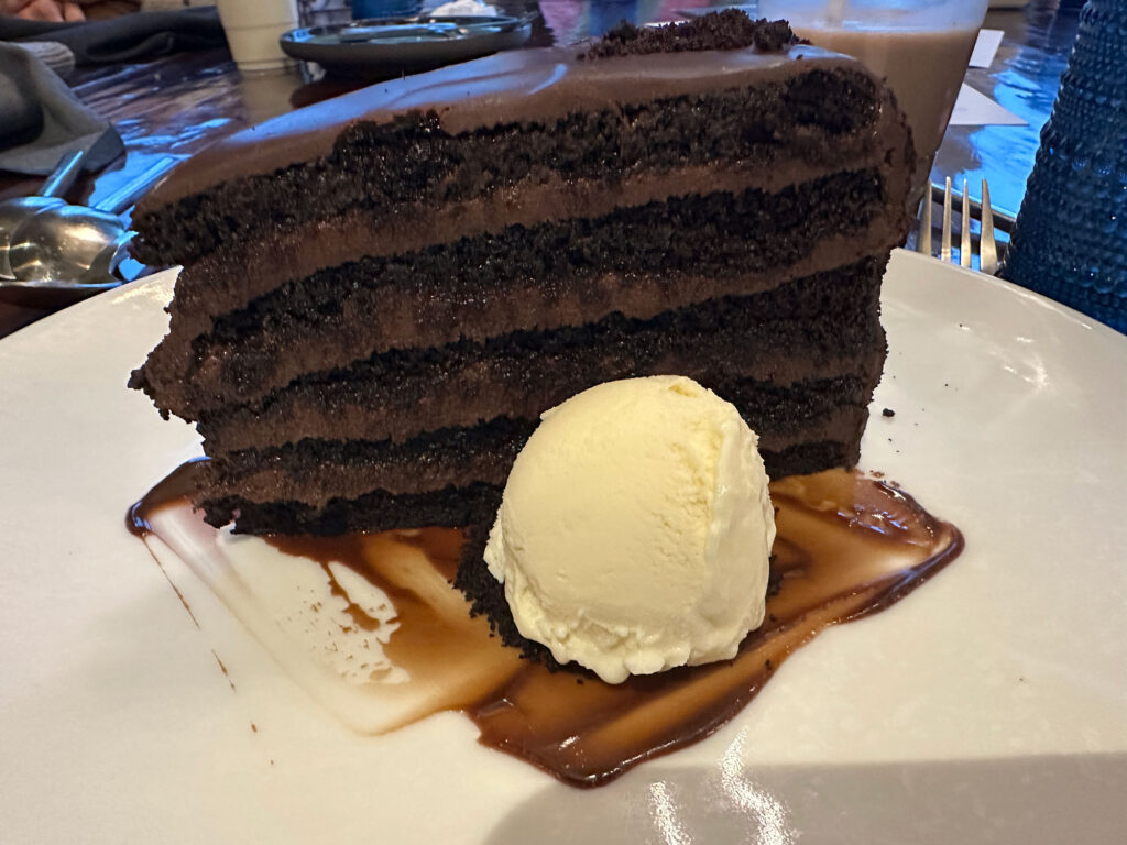 white plate with a tall four-layer chocolate cake next to a small scoop of vanilla ice cream.