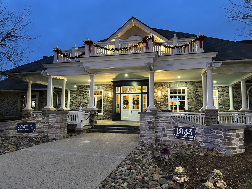 white building with a large porch and two stone walls on either side of an entry walkway. 