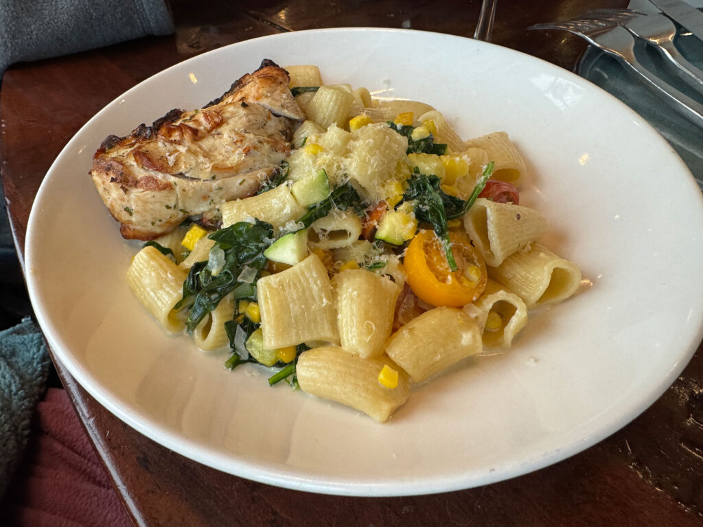 large round white plate with rigatoni noodles tossed with squash and spinach with a chicken breast on top