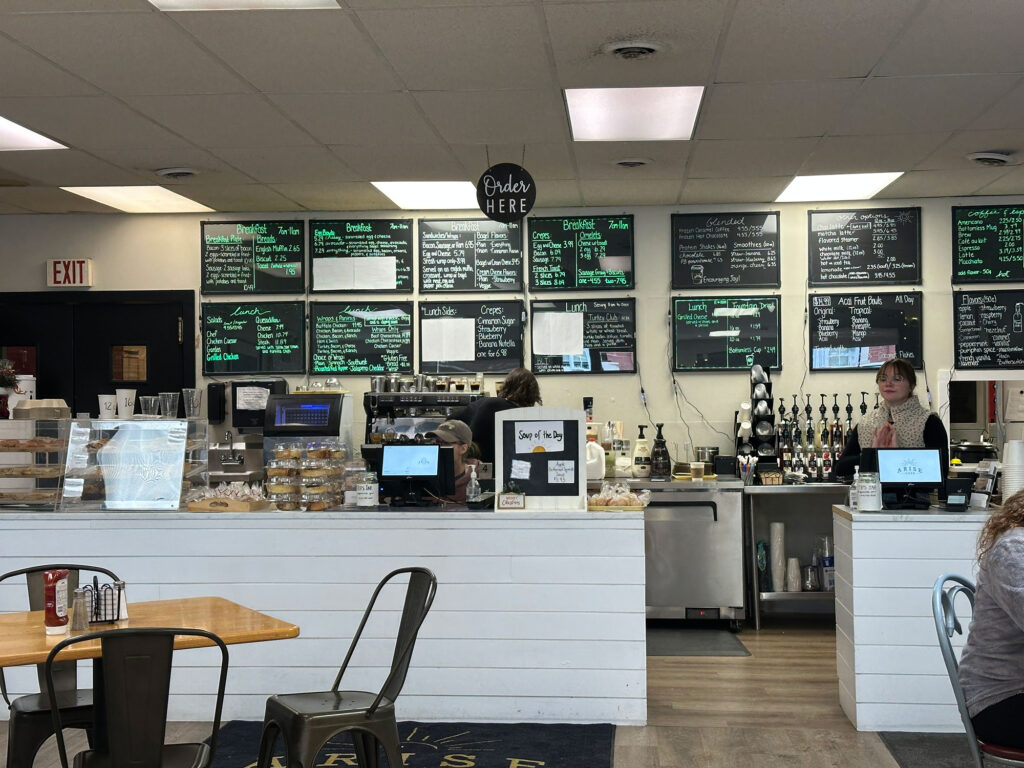 Interior of a cafe with white short wall at the order counter and green lettering on the black menu boards behind