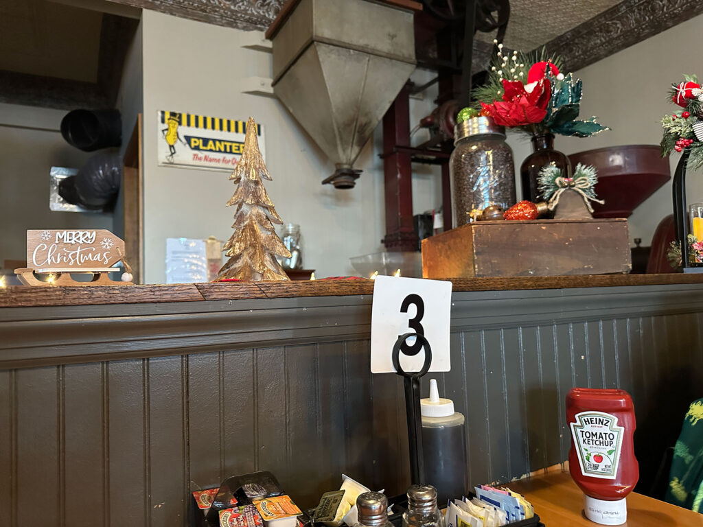 wooden half wall in a dining room with a table number 3 in the foreground and antique coffee roasting equipment in the background.