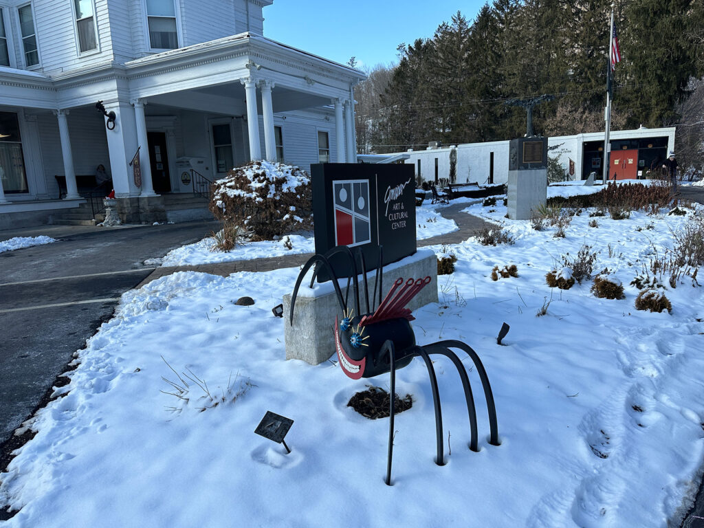 a snowy scene of a spider sculpture next to a sign for the Gmeiner Art & Cultural Center in Wellsboro, PA