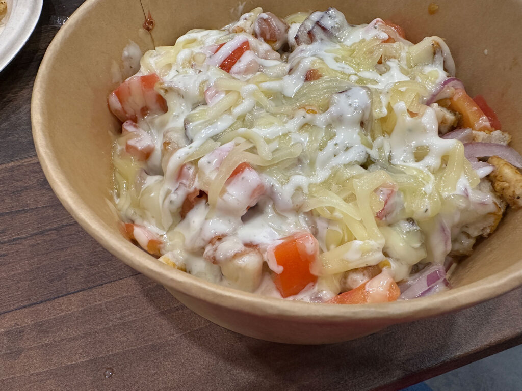 small bowl filled with tater tots topped with grilled chicken, bacon, and ranch dressing