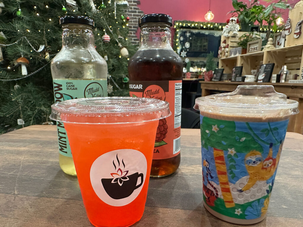 four drinks - two tall glass bottles, one clear plastic cup with red strawberry lemonade, and one holiday kids cup on a table