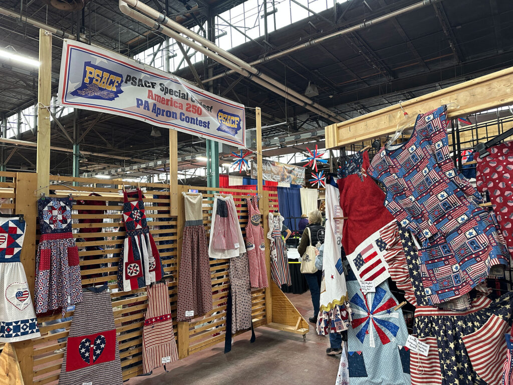 red, whtie, and blue aprons displayed beneath a sign that reads "America 250 Apron Contest"