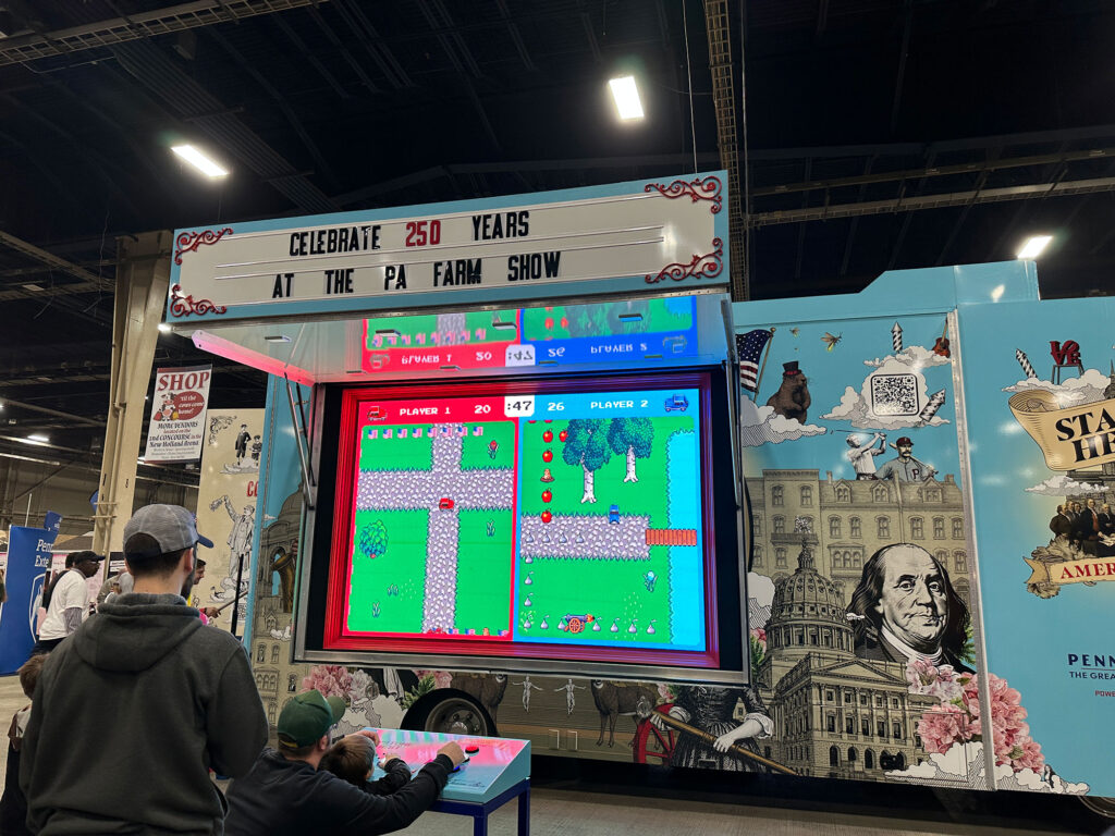 father and son playing a video game that is being projected onto the side of a trailer wrapped to celebrate the America 250th