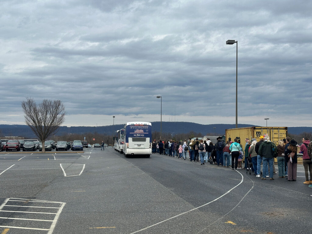 people standing in line for a bus in a large parking lot
