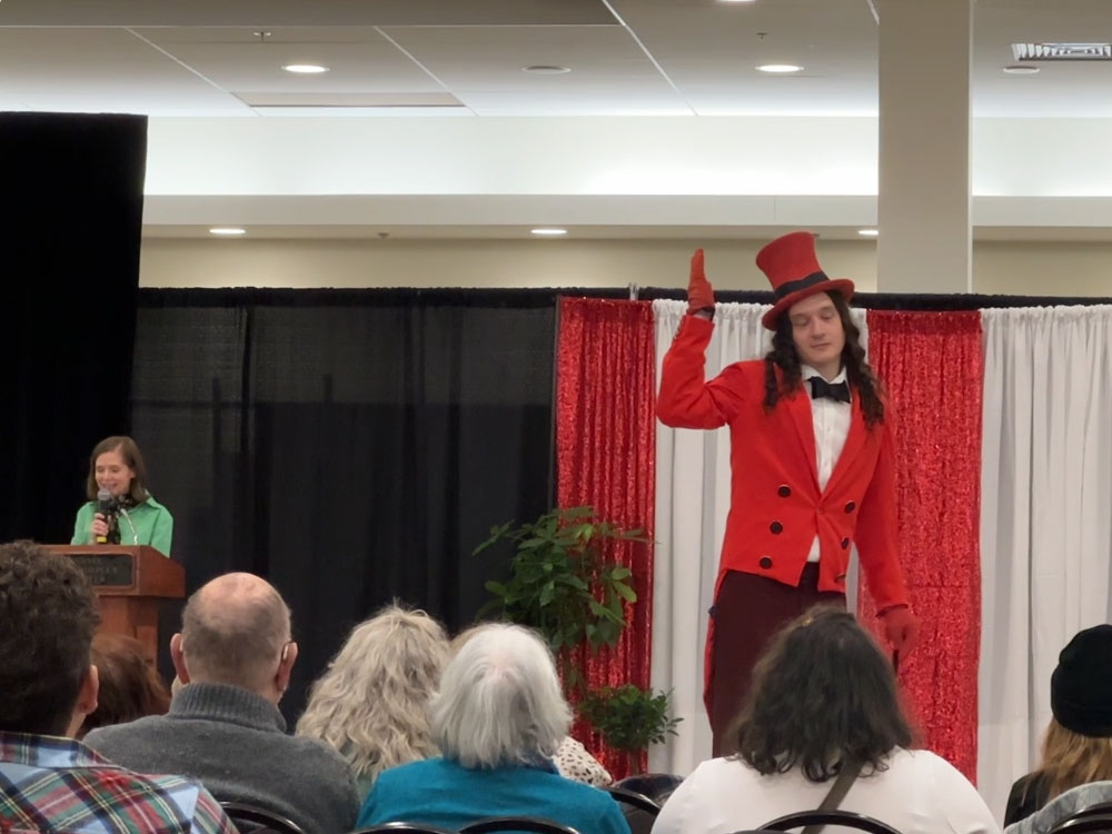 a young man in a red tuxedo and top hat waves to a small crowd of people while modeling the outfit
