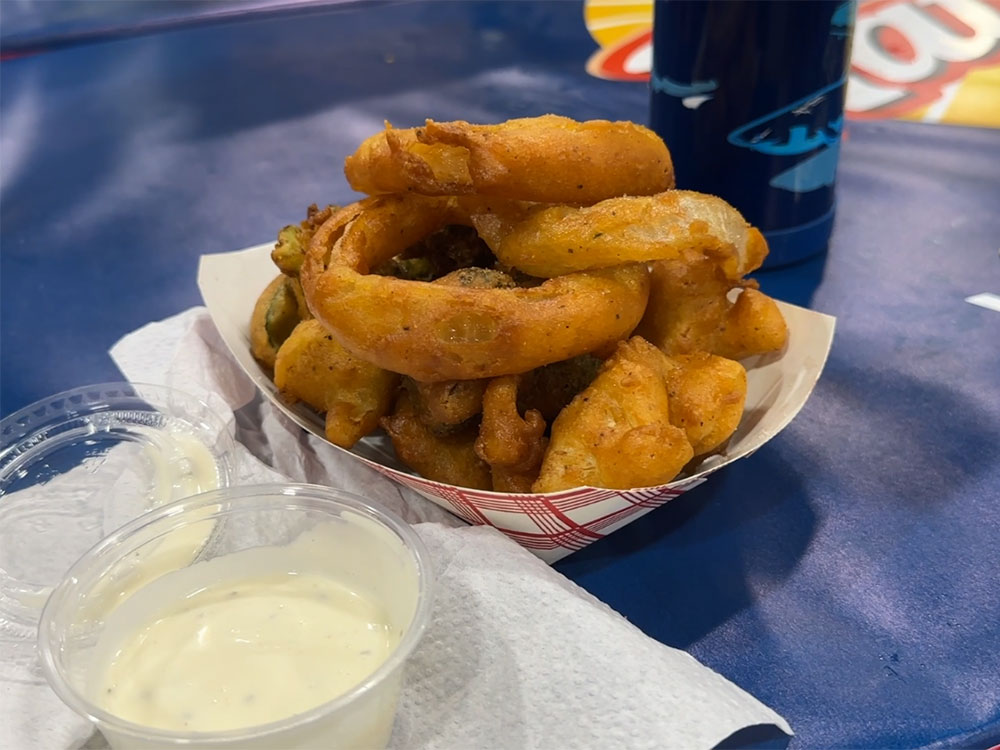 takeout boat filled with fried vegetables next to a cup of ranch dressing for dipping.