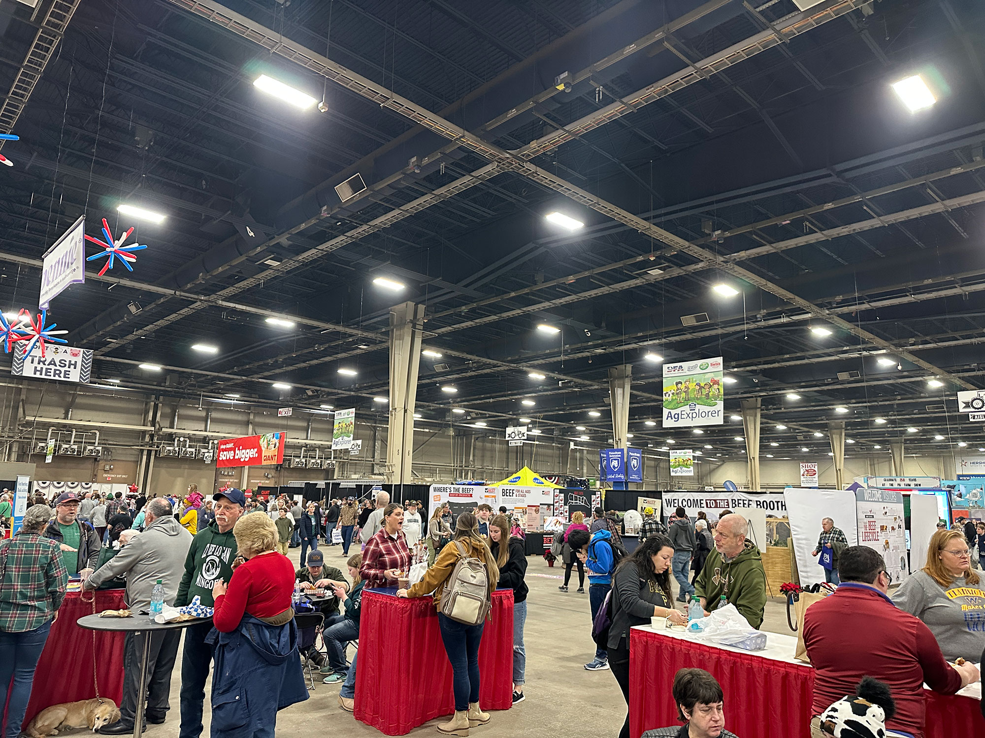 large room filled with people standing at tables with red table cloth