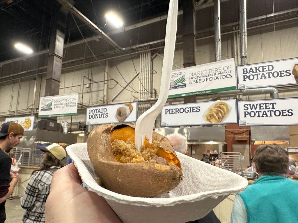 a hand holding up a baked sweet potato with a white plastic fork in it