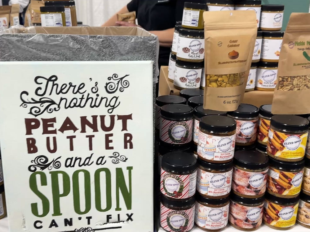 vendor booth with stacked jars of peanut butter and a sign that reads "there's nothing peanut butter and a spoon can't fix."