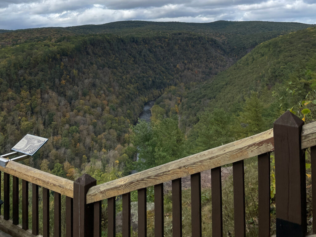 Wooden railing in front of a scenic overlook at the Pennsylvania Grand Canyon on an early fall day with mostly green leaves and some starting to brown. 