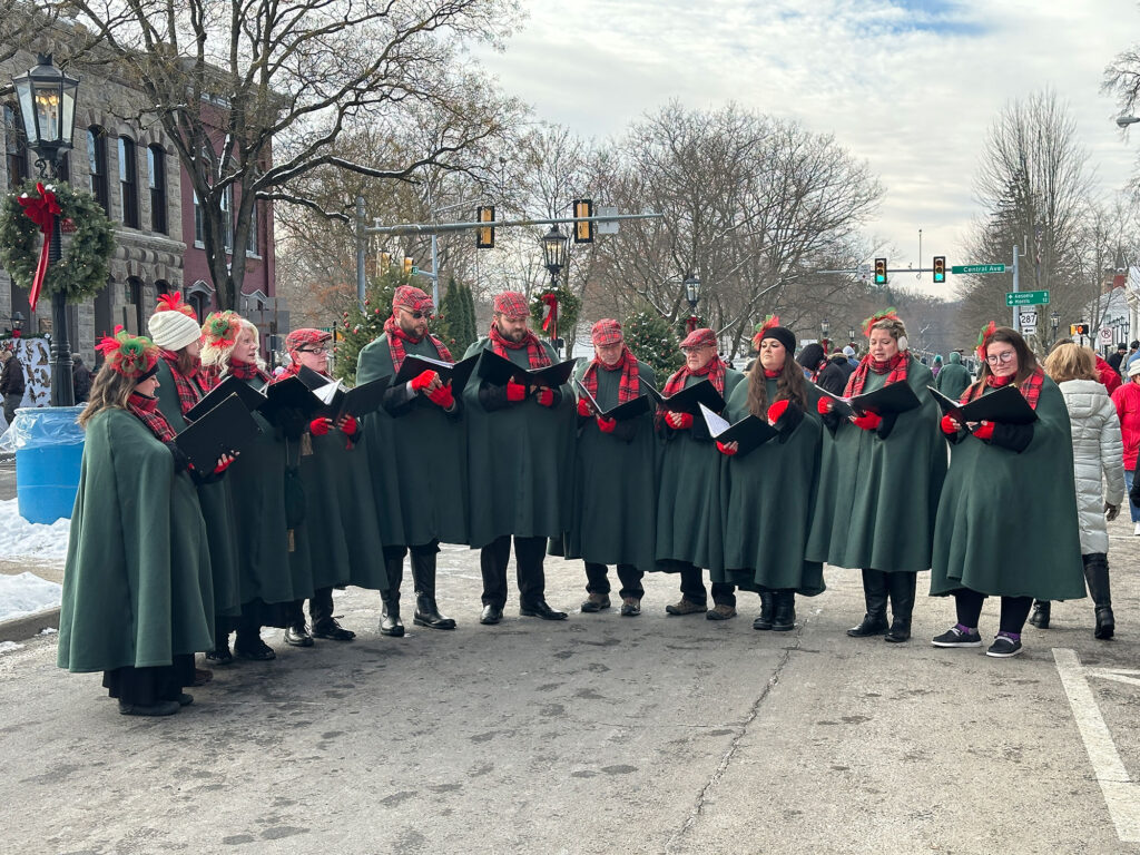 Group of carolers wearing long green coats in Victorian style