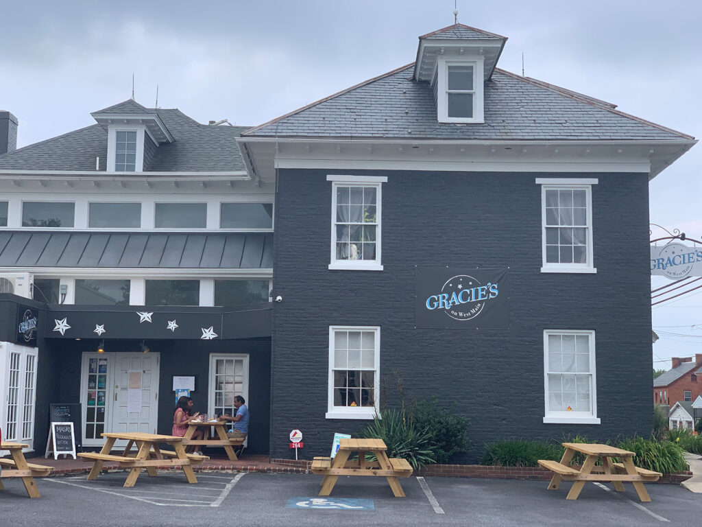 gray-colored farmhouse building with the name "Gracie's" in a circle painted between the first and second floors