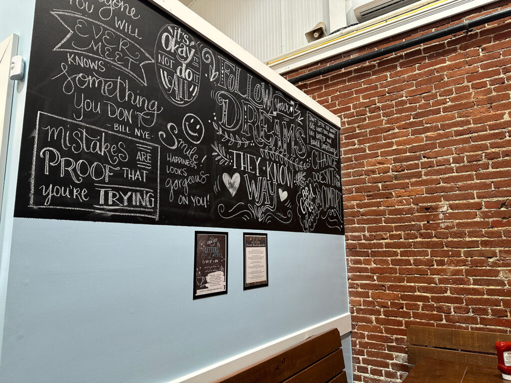 a brick wall meets a blue wall in a corner - the blue wall has a black chalkboard with inspirational sayings scribbled on it