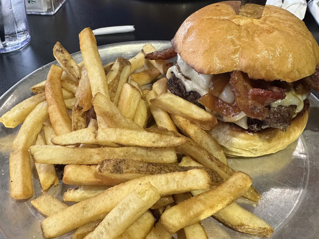metal tray with a pile of fries and a burger topped with bacon and cheese 