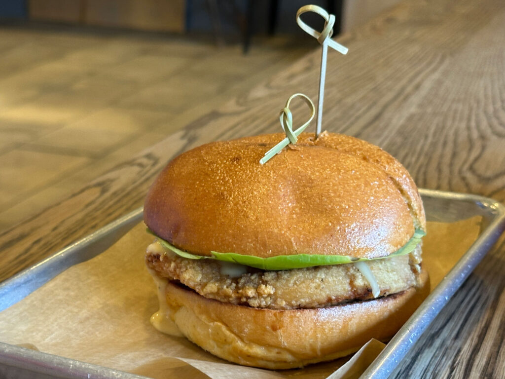 fried chicken sandwich with two toothpicks through the top sitting on a metal tray lined with brown paper