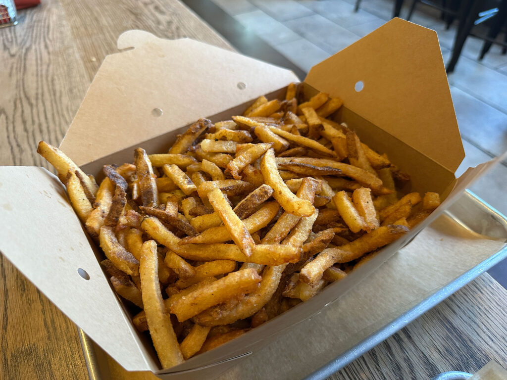 large brown takeout box filled with small, fresh-cut French fries. 