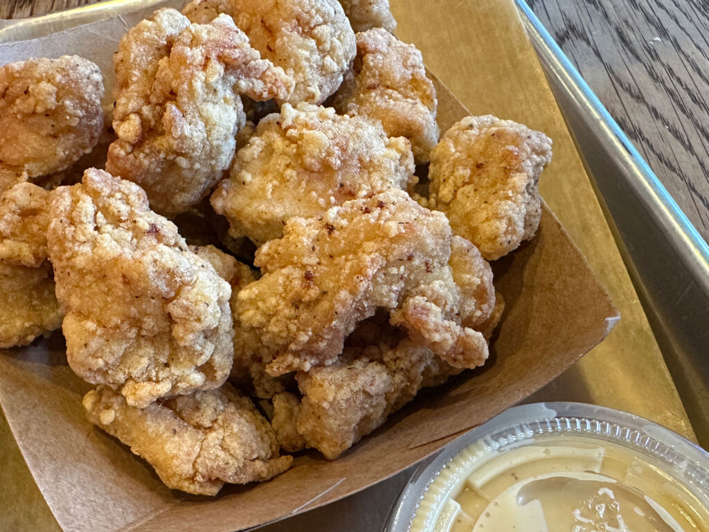 brown paper tray filled with popcorn chicken next to a plastic cup of honey mustard