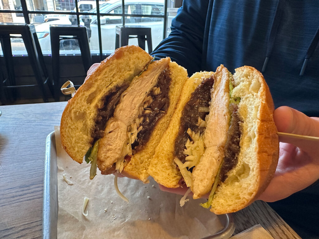 hands holding a sandwich cut in half to show the inside layers of chicken, onion jam, cheese and lettuce