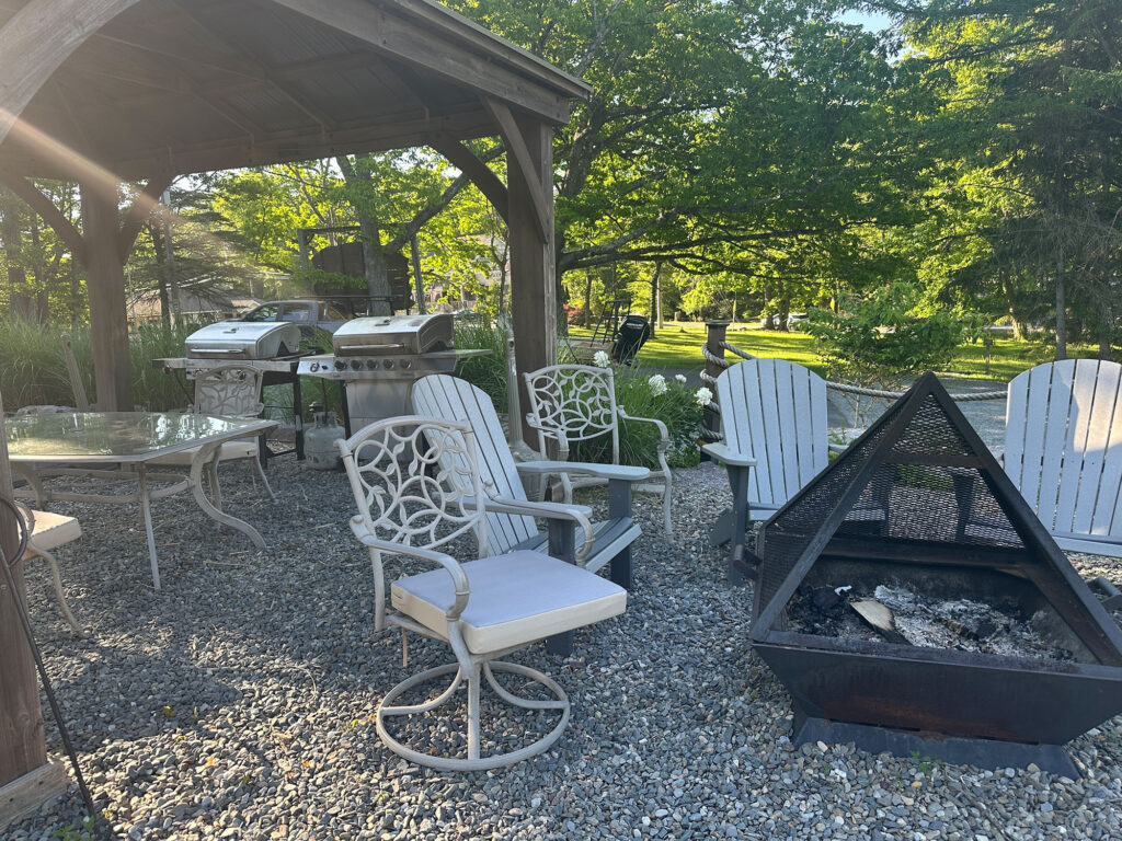 metal chairs surrounding a fire pit with a pavilion with two grills in the background