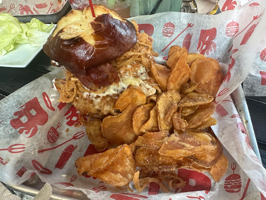 chicken sandwich on a pretzel bun with a chips in a basket